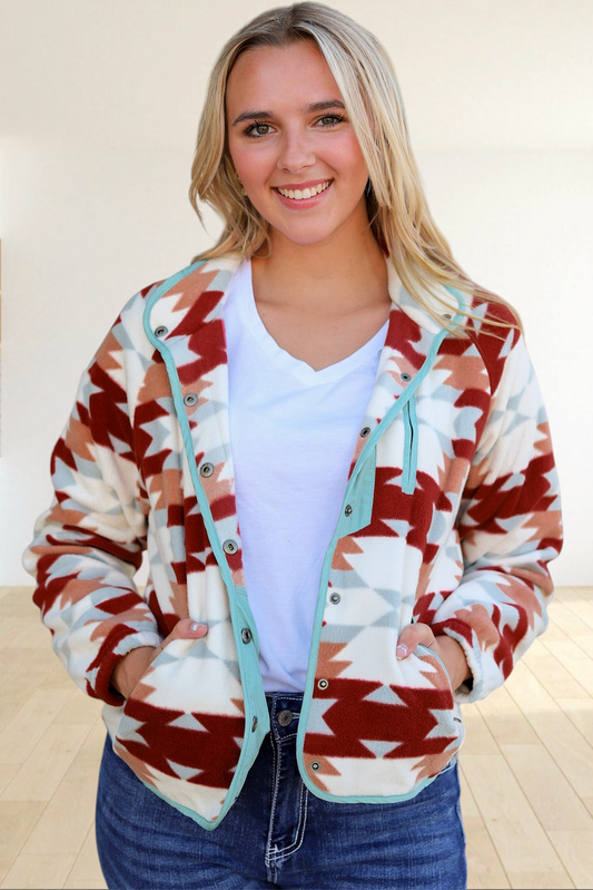 Baya Wear fleece snap jacket with a fiery red and cream Aztec pattern and light blue trim worn by a smiling woman.