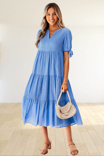 Baya Wear blue textured gingham tiered midi dress with V-neck, short sleeves, and bow-tie details on a smiling model.