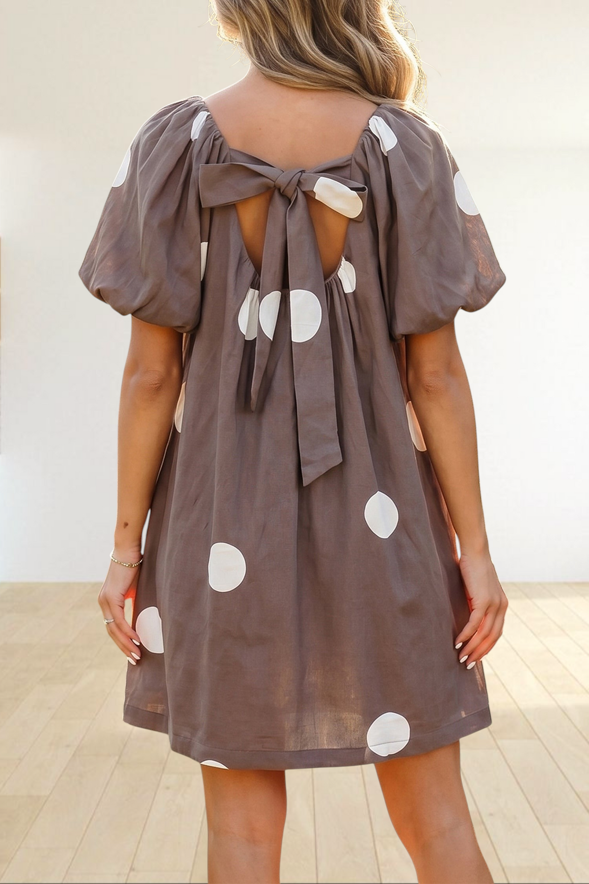 Baya Wear brown mini dress with white polka dots, puff sleeves, and a knot-back detail worn in a garden setting.