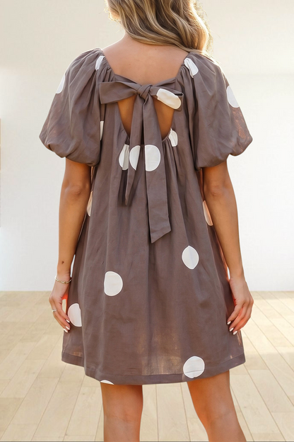 Baya Wear brown mini dress with white polka dots, puff sleeves, and a knot-back detail worn in a garden setting.