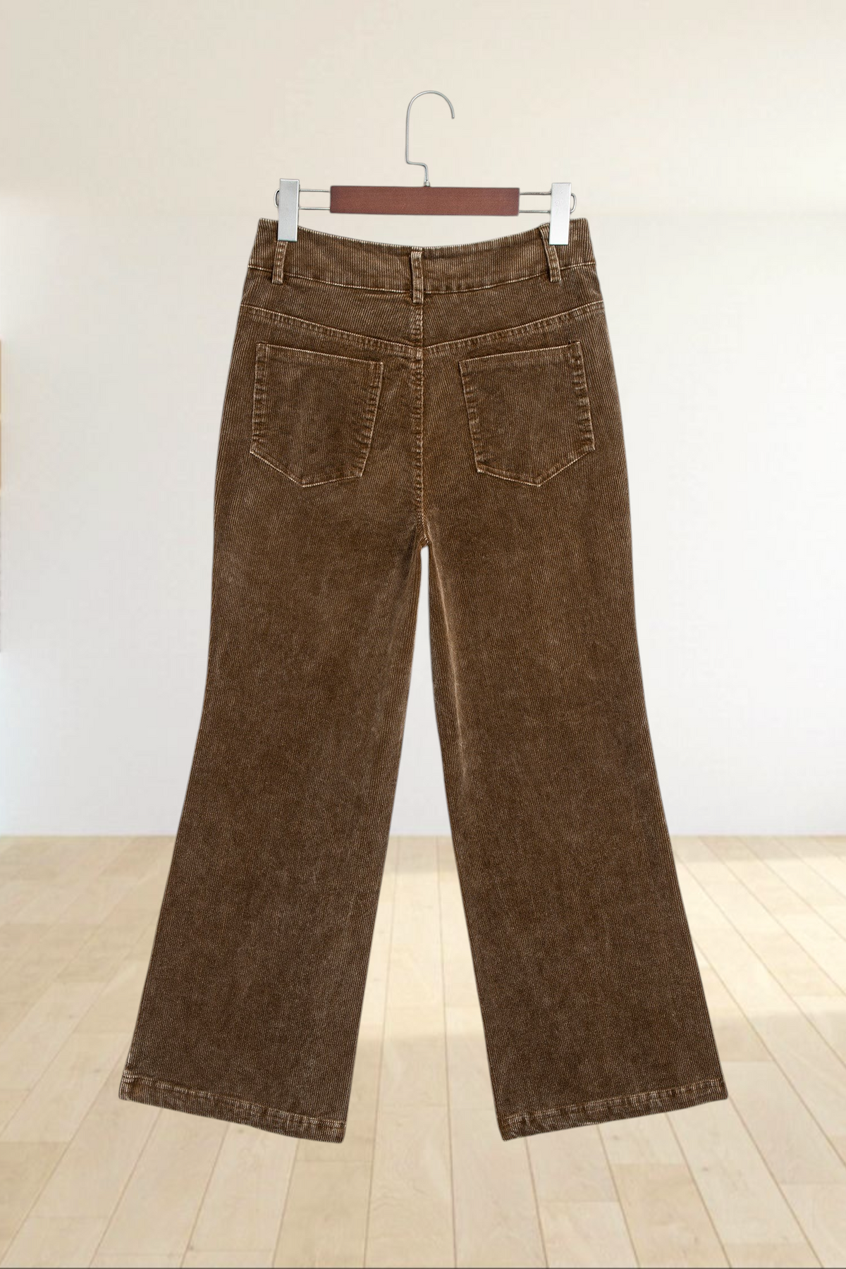 Baya Wear camel corduroy wide leg pants with back pockets hanging on a wooden hanger against a light blue background.