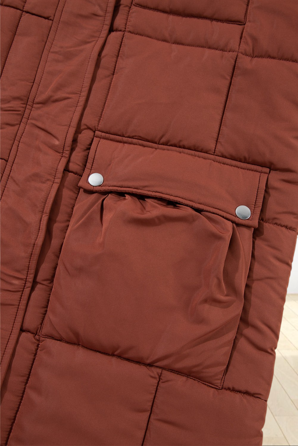 Close-up of a Baya Wear coffee brown quilted puffer jacket featuring a functional flap pocket with silver snap buttons.