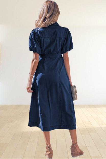 Baya Wear dark blue denim midi dress with puff sleeves and tie-waist belt, worn by a woman on a sunny sidewalk.