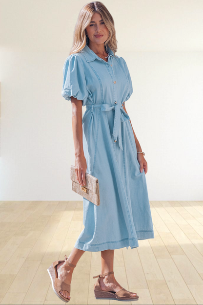 Baya Wear light blue denim midi dress with puff sleeves, button front, and tie-waist belt worn by a woman outdoors.