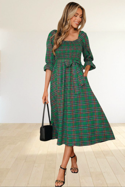 Baya Wear green tartan plaid midi dress with smocked bodice, puff sleeves, and waist tie worn by a woman in a kitchen.