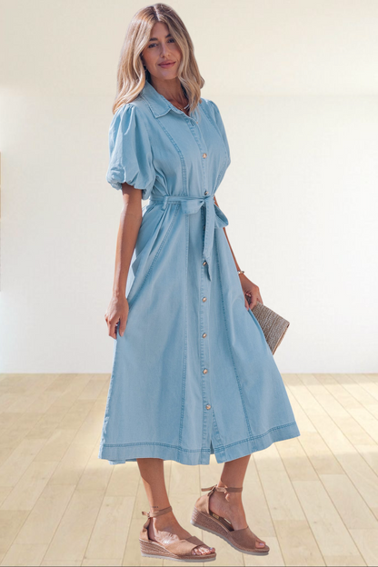A woman wearing a Baya Wear light blue denim midi dress with puff sleeves, a button-down front, and a tie-waist belt.