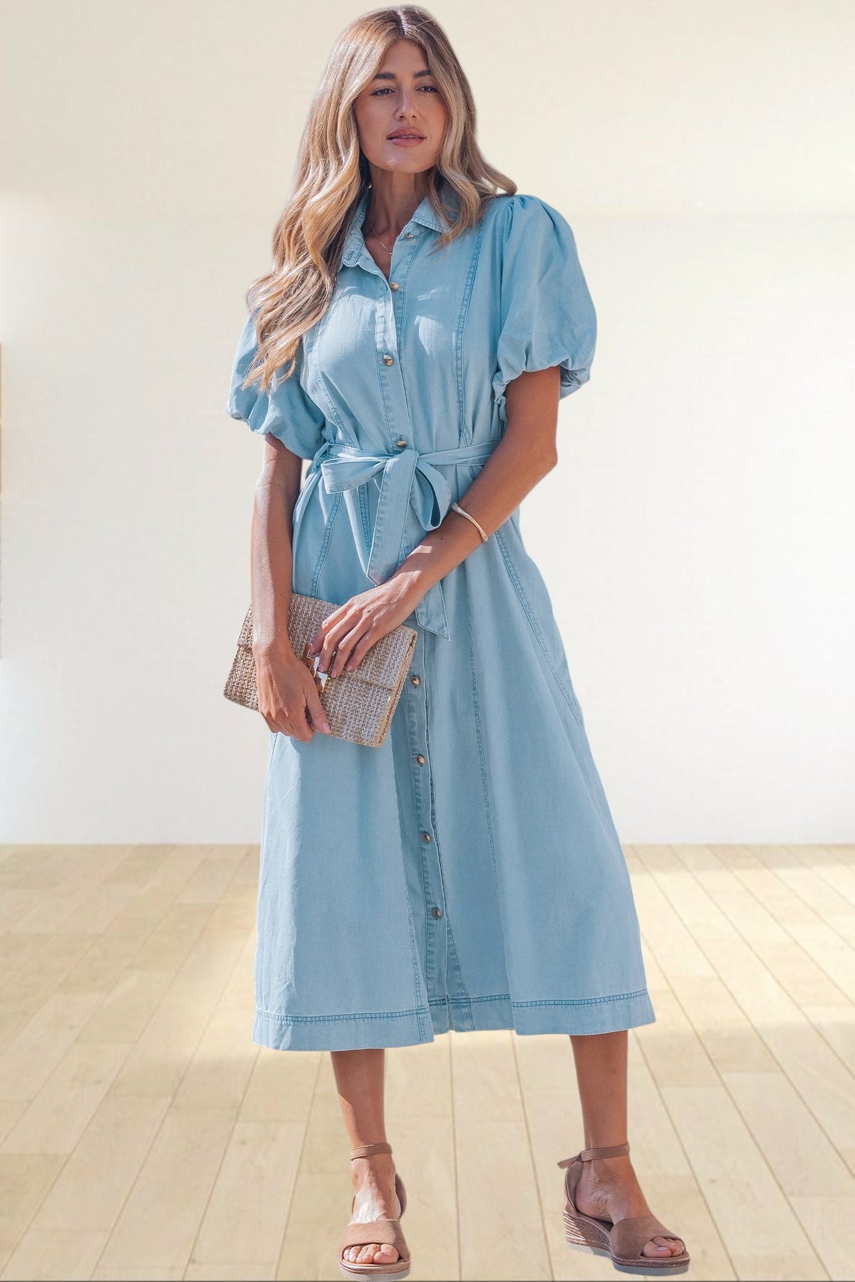 Baya Wear light blue denim midi dress with puff sleeves, button-down front, and tie-waist belt on a woman outdoors.