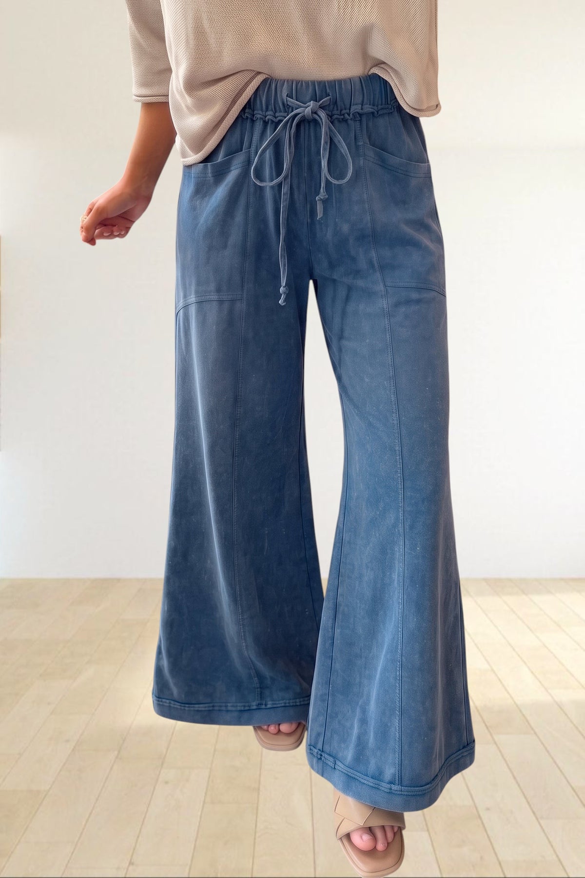 Baya Wear mineral wash blue flare leg lounge pants with drawstring waist and seam details worn with beige sandals.