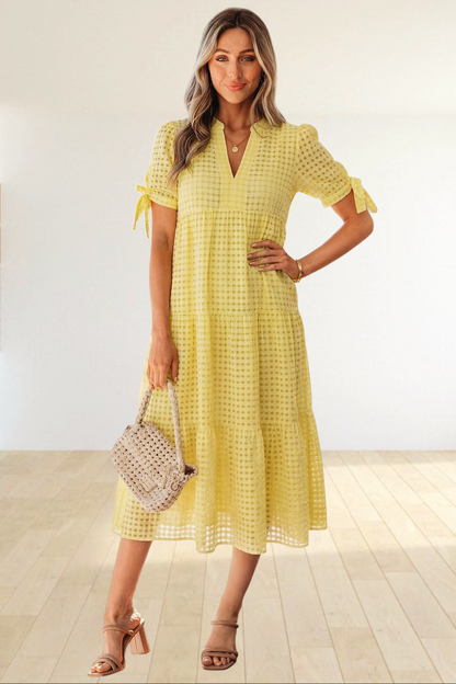 Baya Wear yellow textured gingham tiered midi dress with V-neck, short sleeves, and bow-tie details on a model.