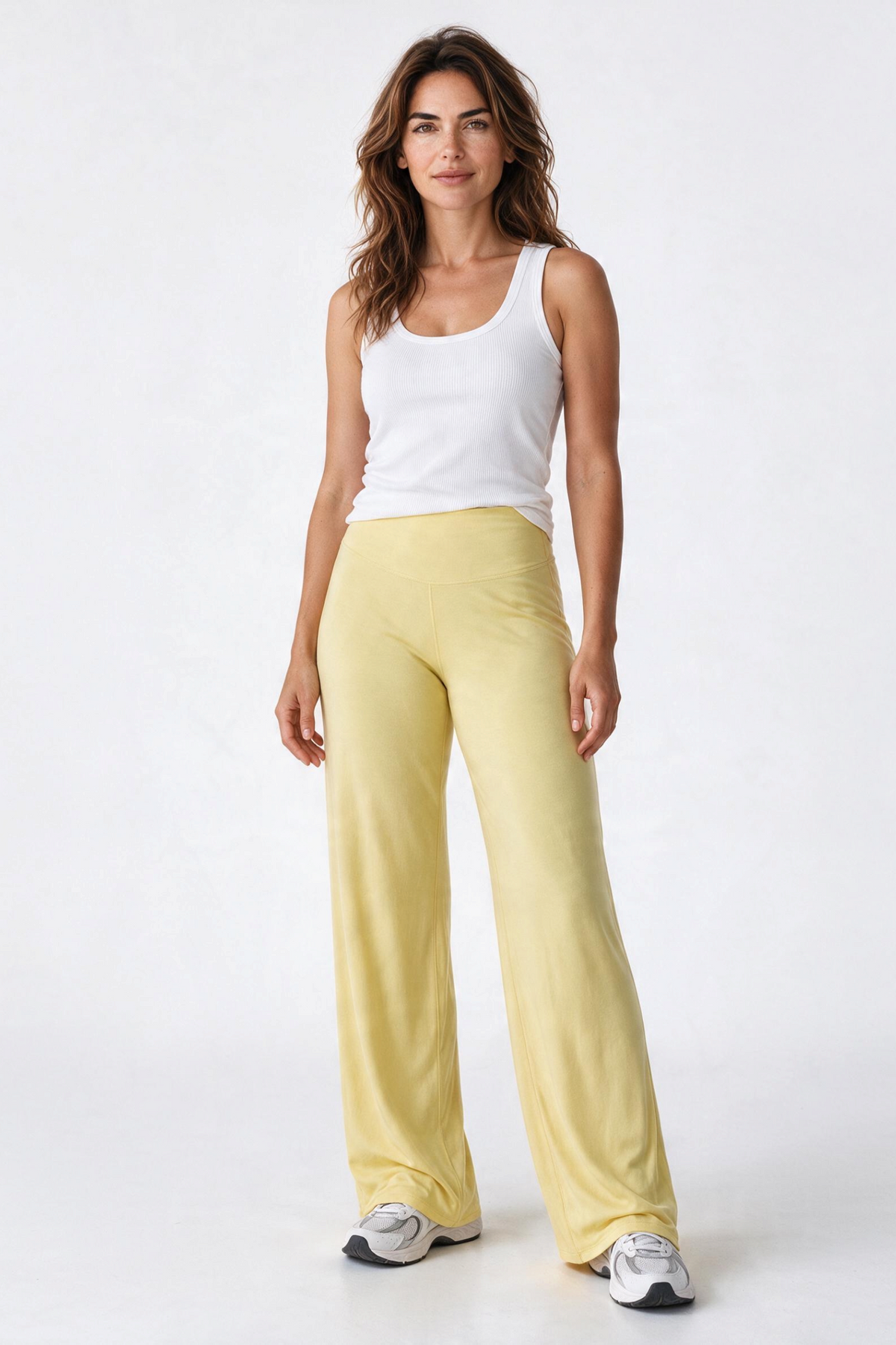 Baya Wear model wearing high-waisted yellow wide-leg yoga pants with a white tank top against a white background